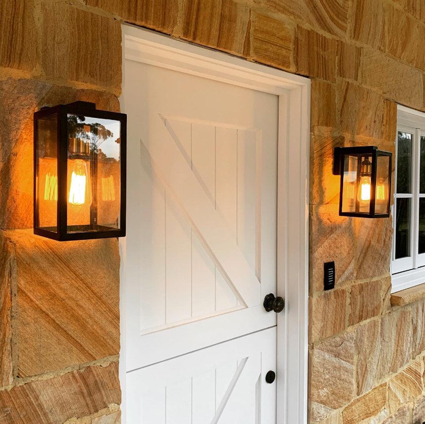 Lantern wall lights either side of a white stable door on a sandstone home